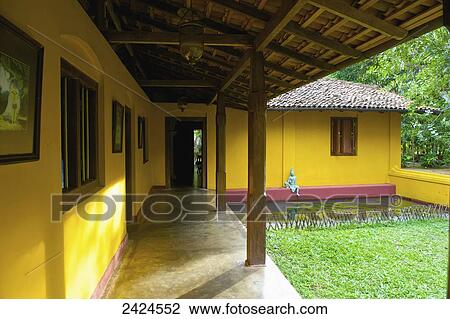 Stock Image - A bright yellow building with a statue sitting on a red ledge by a pond; Ulpotha, Embogama, Sri Lanka. Fotosearch
