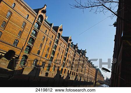 Stock Image - A brown brick building along a canal under a blue sky; Hamburg, Germany. Fotosearch