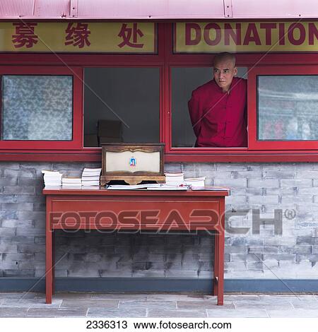 Stock Image - A Buddhist Monk Stands In A Window Taking Donations At Lama Temple; Beijing, China. Fotosearch