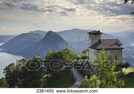 Stock Image - A building at high elevation overlooking the mountains and lakes; Lugano, Ticino, Switzerland. Fotosearch