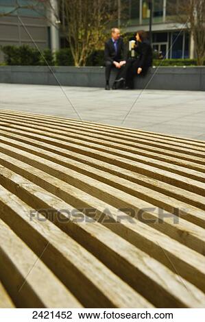 Stock Image - A businessman and businesswoman sit on a ledge talking outside a building, Spitalfields; London, England. Fotosearch