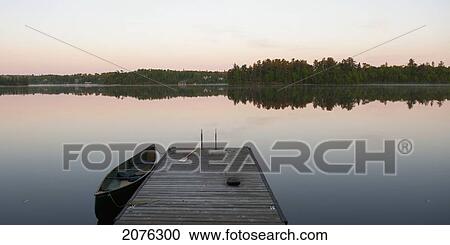 Stock Image - A Canoe In The Water Beside A Dock At Sunset; Lake Of The Woods Ontario Canada. Fotosearch