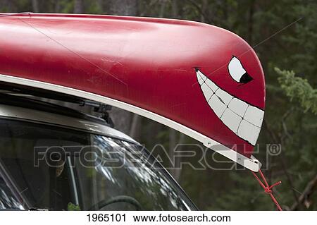Stock Image - A Canoe With A Painted Face On The Front Is Strapped To A Vehicle; Alberta Canada. Fotosearch