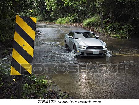 Stock Image - A car driving through a shallow stream on the North Shore at Ha'ena Beach Park; Kauai, Hawaii, United States of America. Fotosearch
