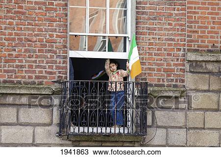 Stock Image - A Child Stands At The Window Watching The Saint Patrick's Day Parade; Dublin Ireland. Fotosearch