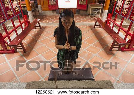Stock Image - A Chinese young woman praying and offering incense in a Buddhist temple; Shanzidou, Kinmen Island, Taiwan. Fotosearch
