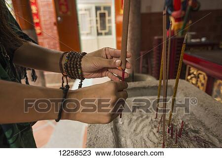 Stock Image - A Chinese young woman praying and offering incense in a Buddhist temple; Shanzidou, Kinmen Island, Taiwan. Fotosearch