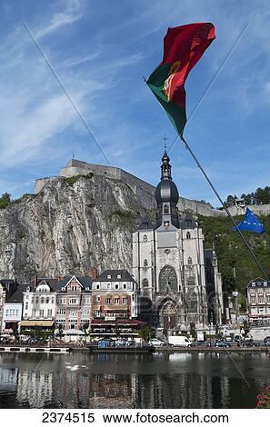 Stock Photography - A church and other buildings along the water and flags flying; Dinant, Belgium. Fotosearch