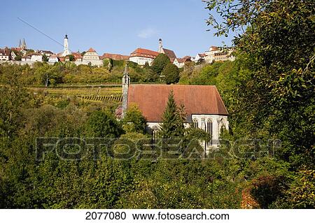 Stock Image - A Church Surrounded By Trees And Other Buildings In The Background; Rothenburg Ob Der Tauber Bavaria Germany. Fotosearch