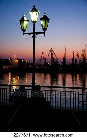 Stock Image - A classical style street lamp and the cargo cranes of Odessa port at sunset; Odessa, Ukraine. Fotosearch