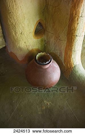 Stock Image - A clay jar stands against a cracked interior wall; Ulpotha, Embogama, Sri Lanka. Fotosearch