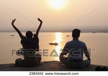 A couple does yoga and meditates at sunset overlooking the River Ganges; Varanasi, Uttar Pradesh State, India View Large Photo Image Stock Photography - A couple does yoga and meditates at sunset overlooking the River Ganges; Varanasi, Uttar Pradesh State, India. Fotosearch