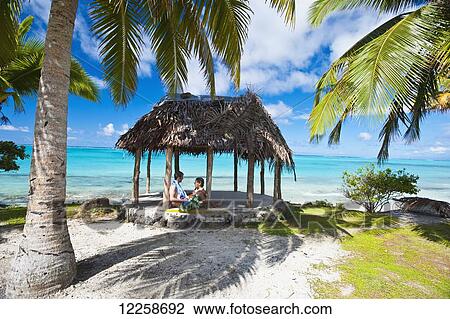 Stock Image - A couple in a beach fale (hut); Savaii Island, Samoa. Fotosearch