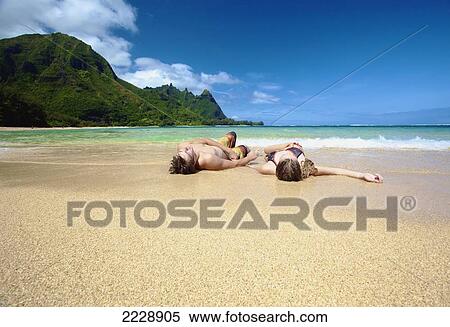 Stock Photography - A couple laying in the sand at the water's edge; Wailua, Hawaii, United States of America. Fotosearch
