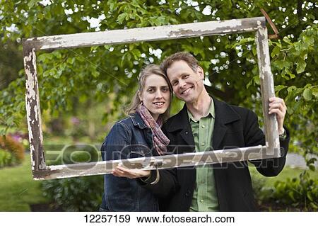 A couple posing for a portrait holding a wooden frame around their faces; Vancouver, British Columbia, Canada View Large Photo Image Stock Photo - A couple posing for a portrait holding a wooden frame around their faces; Vancouver, British Columbia, Canada. Fotosearch