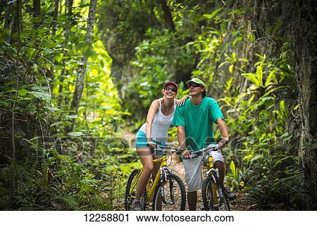 A couple riding their bicycles on a trail through a lush forest; Niue View Large Photo Image Stock Image - A couple riding their bicycles on a trail through a lush forest; Niue. Fotosearch
