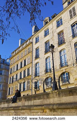 Stock Photograph - A couple sit together on a wall beside a lamp post in front of a residential building; Paris, France. Fotosearch