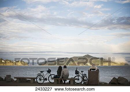 Stock Photo - A couple sits by San Francisco Bay as the sun sets; San Francisco, California, United States of America. Fotosearch