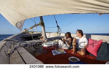 Stock Photograph - A couple sits enjoying a meal on a sailboat; Vamizi Island, Mozambique. Fotosearch