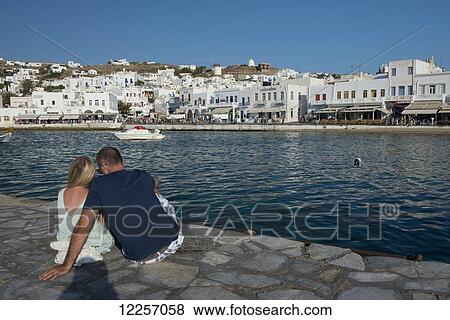 Stock Photo - A couple sitting on a stone pier in Mykonos Harbour; Mykonos Town, Mykonos, Cyclades, Greek Islands, Greece. Fotosearch