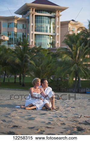 Stock Photography - A couple sitting on the beach at the Empire Hotel and Country Club; Bandar Seri Begawan, Brunei. Fotosearch
