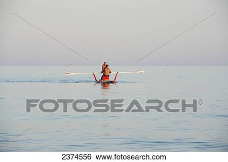 Stock Photograph - A couple standing together in a boat with a long paddle; Puglia, Italy. Fotosearch
