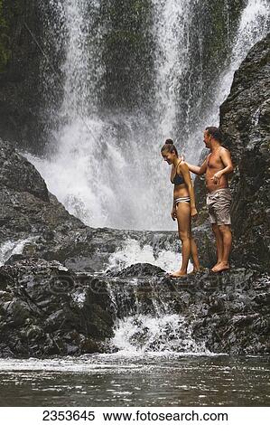 Stock Photography - A Couple Stands By The Gorgeous Piroa Falls By The Waipu Gorge; Waipu, New Zealand. Fotosearch