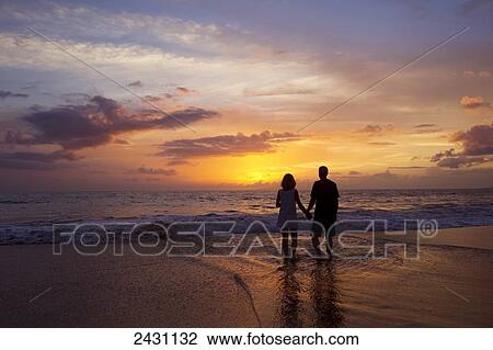 Stock Image - A couple stands on the beach at sunset; Wailea, Maui, Hawaii, United States of America. Fotosearch