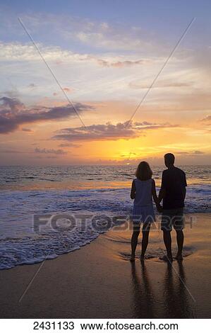 Stock Image - A couple stands on the beach at sunset; Wailea, Maui, Hawaii, United States of America. Fotosearch