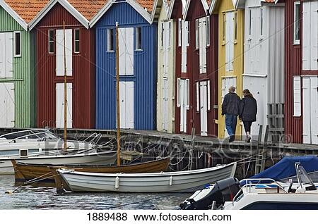Stock Photo - A Couple Strolling Past The Colourful Fishing Huts Along The Quayside At Smogen.. Fotosearch