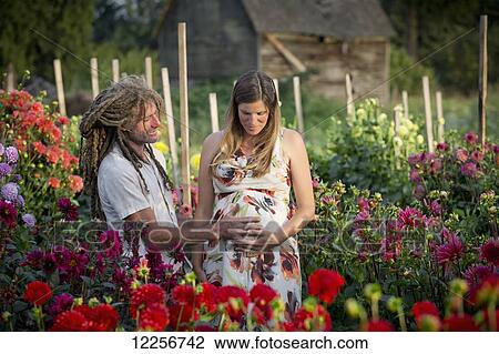 Stock Image - A couple touching the woman's pregnant belly while standing in a flower garden; Abbotsford, British Columbia, Canada. Fotosearch