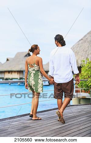 Stock Image - A Couple Walks Along A Boardwalk In The Bora Bora Nui Resort & Spa; Bora Bora Island Society Islands French Polynesia South Pacific. Fotosearch