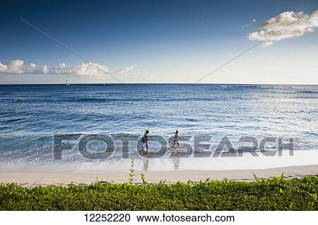 Stock Image - A couple walks along the popular tourist beach; Poipu, Kauai, Hawaii, United States of America. Fotosearch