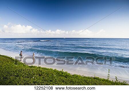 Stock Photo - A couple walks along the popular tourist beach of Poipu; Poipu, Kauai, Hawaii, United States of America. Fotosearch