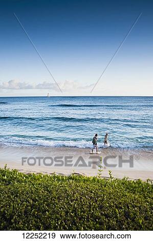Stock Photo - A couple walks along the popular tourist beach; Poipu, Kauai, Hawaii, United States of America. Fotosearch