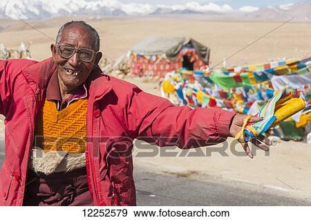 Stock Photo - A crazy nomad dancing, Tibetan flags in his hands, showing us his happiness that he lives there, Tibetan Friendship Highway; Tibet, China. Fotosearch