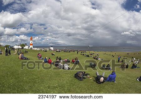 A crowd gathered on the grass along the coast with a view of a ship and boats in the water and Souter Lighthouse; Marsden, Tyne and Wear, England View Large Photo Image Stock Photo - A crowd gathered on the grass along the coast with a view of a ship and boats in the water and Souter Lighthouse; Marsden, Tyne and Wear, England. Fotosearch