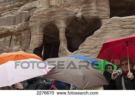 Stock Image - A crowd of tourists shelter under umbrellas during a rain storm at the Unesco World Heritage Site of Petra, one of the new Seven Wonders of the World; Petra, Jordan. Fotosearch