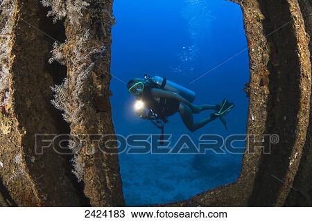 Stock Image - A diver with a hand light outside of the wreck of the YO-257 off Waikiki Beach; Oahu, Hawaii, United States of America. Fotosearch
