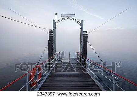 Stock Photo - A Dock Leading Out To Fog Over Lake Maggiore; Locarno, Ticino, Switzerland. Fotosearch