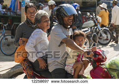 Stock Photo - A family of four ride on a motorcycle at the Old Market; Battambang, Cambodia. Fotosearch