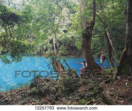 Stock Image - A family standing at a blue hole; Efate Island, Vanuatu. Fotosearch