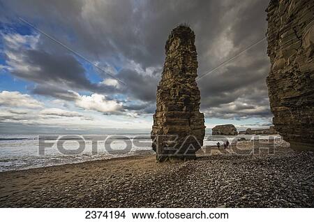 Picture - A family walks on the beach along the water with a tall rock column; South Shields, Tyne and Wear, England. Fotosearch