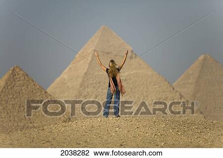 Stock Image - A Female Tourist Raises Her Arms And Looks Out Toward The Pyramids Of Giza Near Cairo; Giza Egypt. Fotosearch