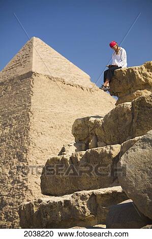 A Female Tourist Reads A Guide Book While Sitting In Front Of The Pyramids Of Giza Near Cairo; Giza Egypt View Large Photo Image Stock Image - A Female Tourist Reads A Guide Book While Sitting In Front Of The Pyramids Of Giza Near Cairo; Giza Egypt. Fotosearch