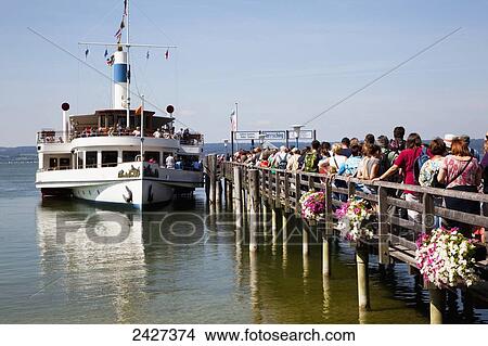 Picture - A ferry arrives at a pier to pick up waiting passengers; Herrsching, Bayern, Germany. Fotosearch