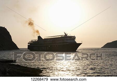 Stock Photo - A ferry in silhouette at sunset arriving in Kamares; Kamares, Sifnos, Cyclades, Greek Islands, Greece. Fotosearch