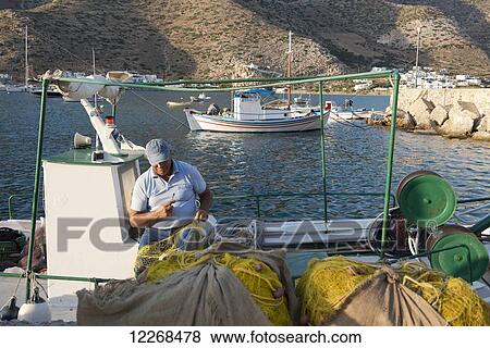Stock Photo - A fisherman repairing his nets in the harbour; Kamares, Sifnos, Cyclades, Greek Islands, Greece. Fotosearch