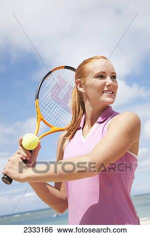 Stock Photograph - A girl at the water's edge with a tennis ball and racquet; Oahu, Hawaii, United States of America. Fotosearch