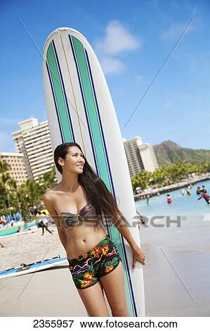 A girl in a bikini standing on the beach with her surfboard; Oahu, Hawaii, United States of America View Large Photo Image Stock Photo - A girl in a bikini standing on the beach with her surfboard; Oahu, Hawaii, United States of America. Fotosearch
